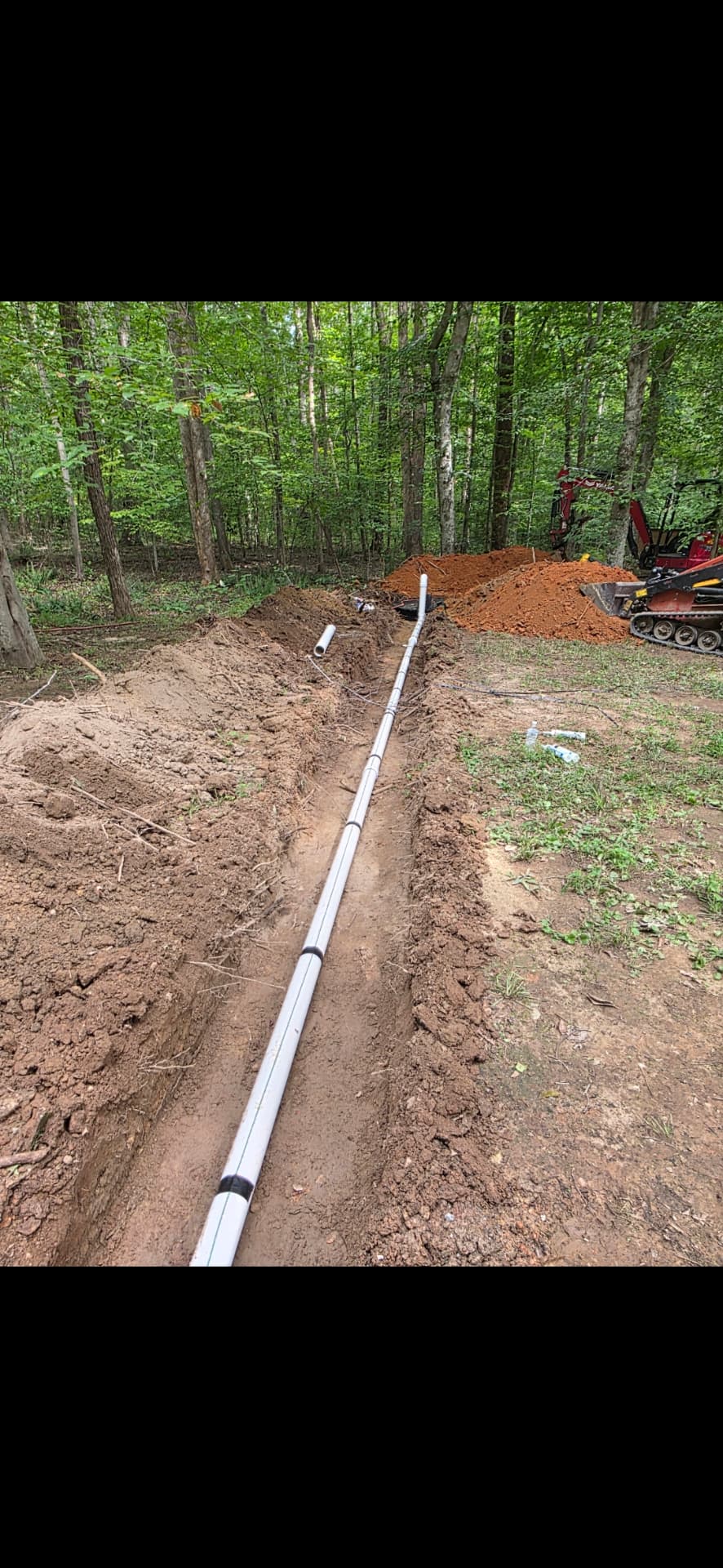 New water service line laid in an open trench through a wooded property